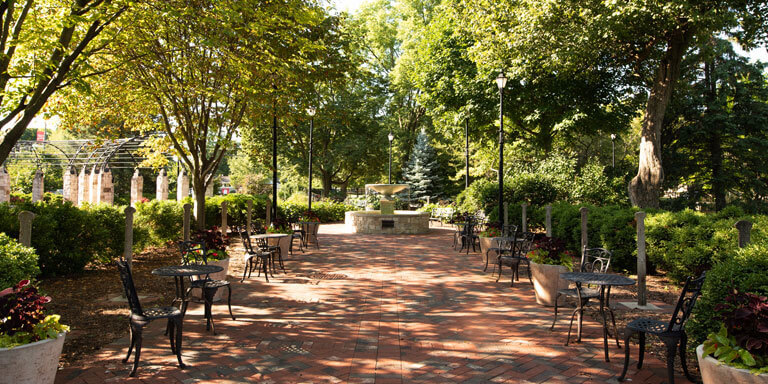 A brick path in the garden is lined with flowers and small bistro tables.