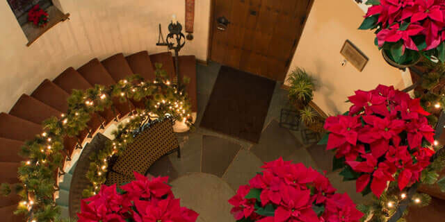 The spiral staircase decorated with poinsettas, lights, and garland.