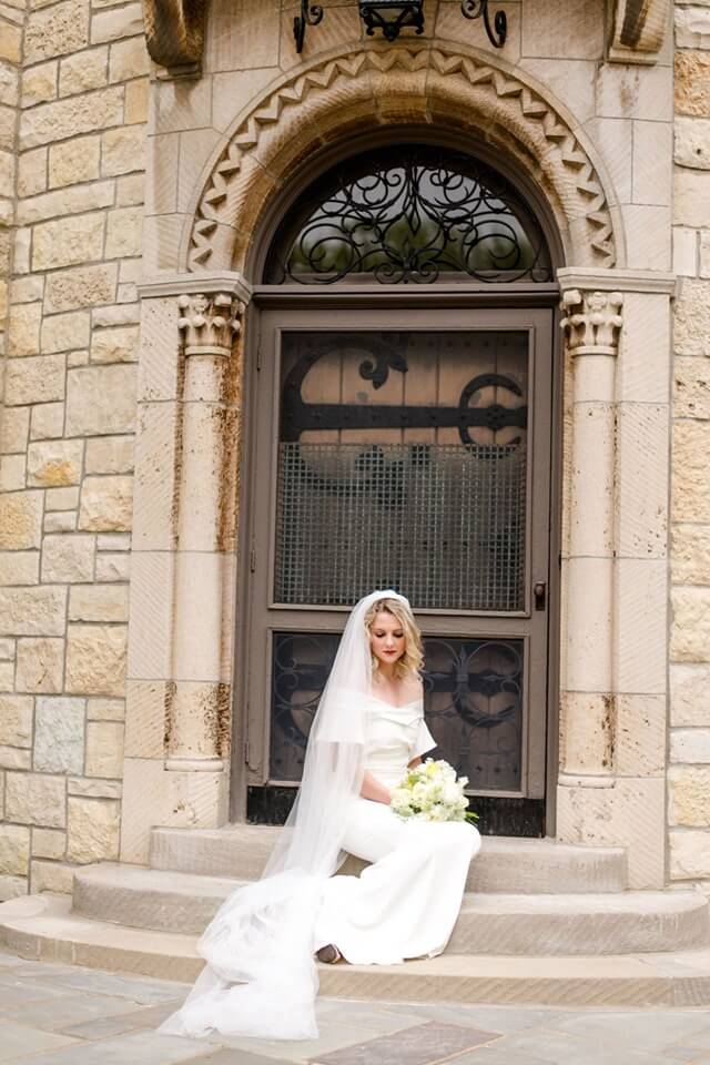 Bride seated on a stairs in front of a door.