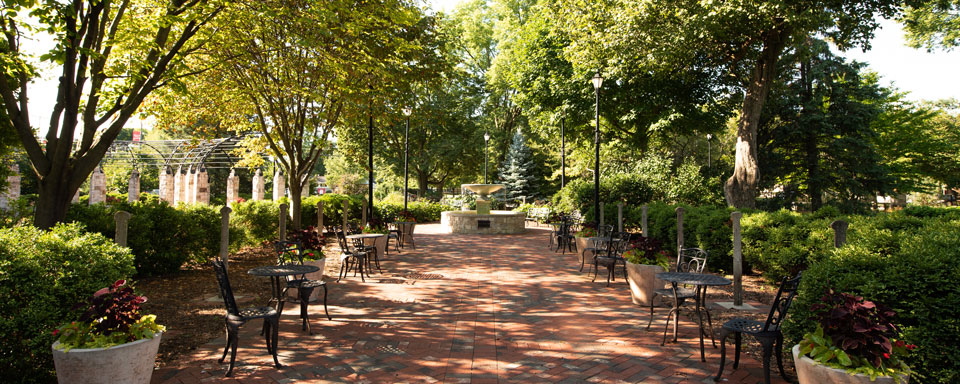 A brick path in the garden is lined with flowers and small bistro tables.