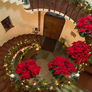 The spiral staircase decorated with poinsettas, lights, and garland.