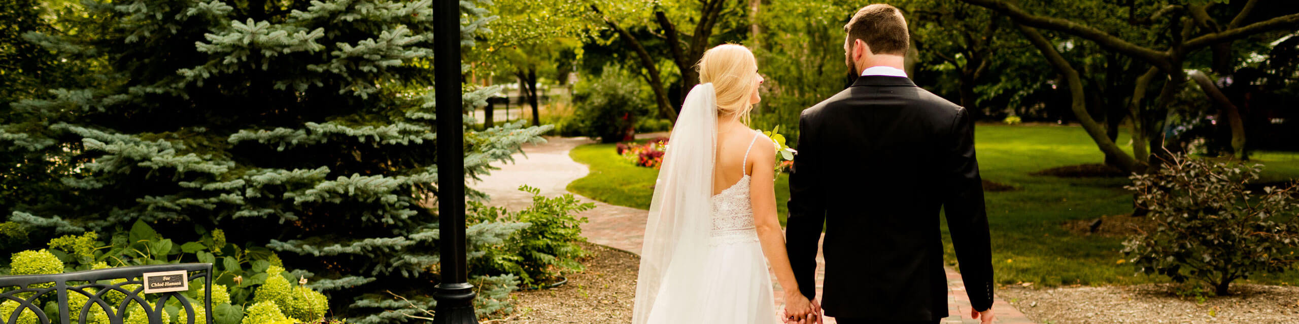 Bride and groom are holding hands and walking on a pathway outside the manor.