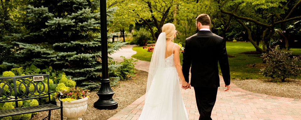 Bride and groom are holding hands and walking on a pathway outside the manor.